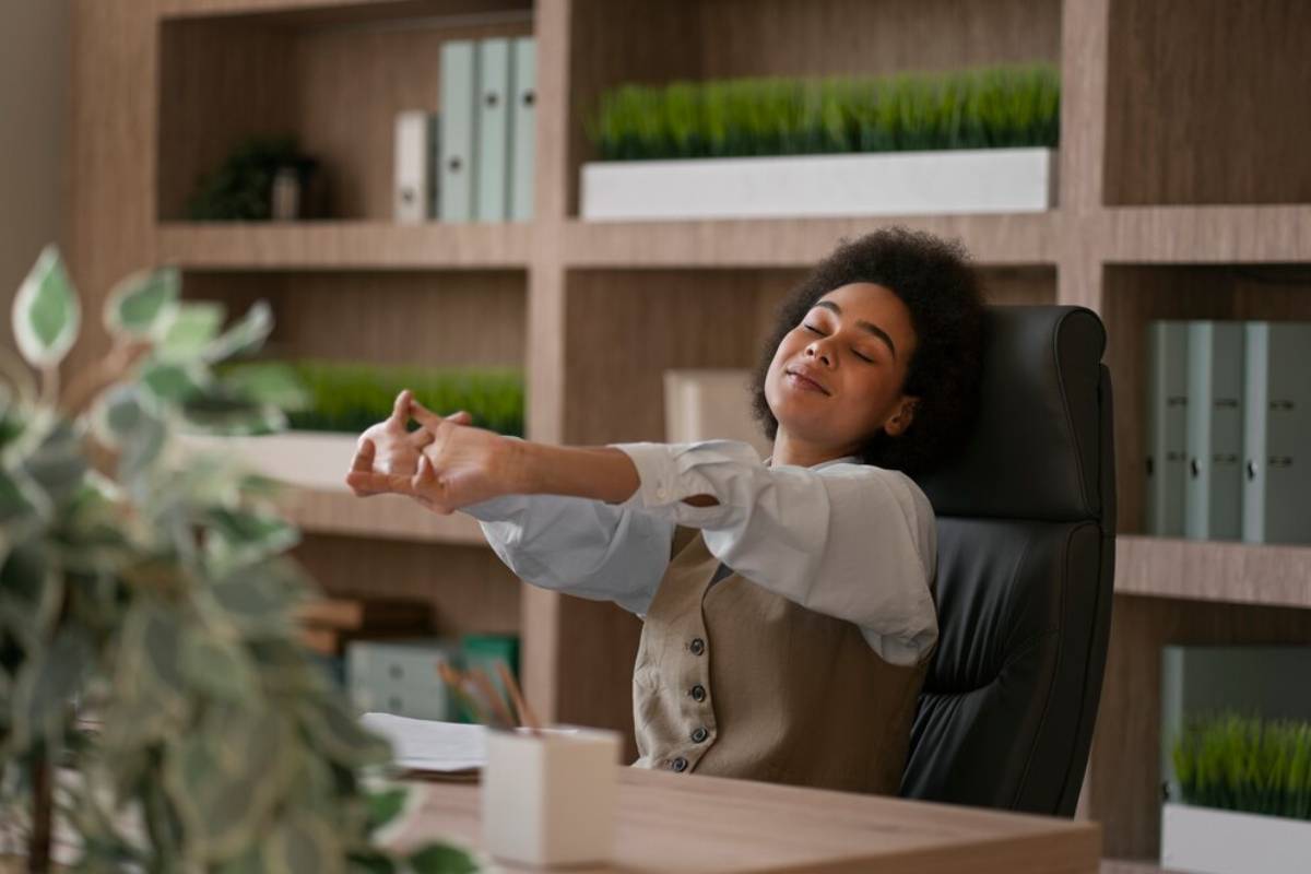 Young woman relaxing and stretching in her office chair, surrounded by plants and a calm workspace.