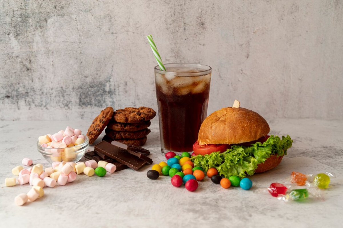 A variety of snacks including a sandwich, cookies, marshmallows, chocolate, and candies on a textured background.