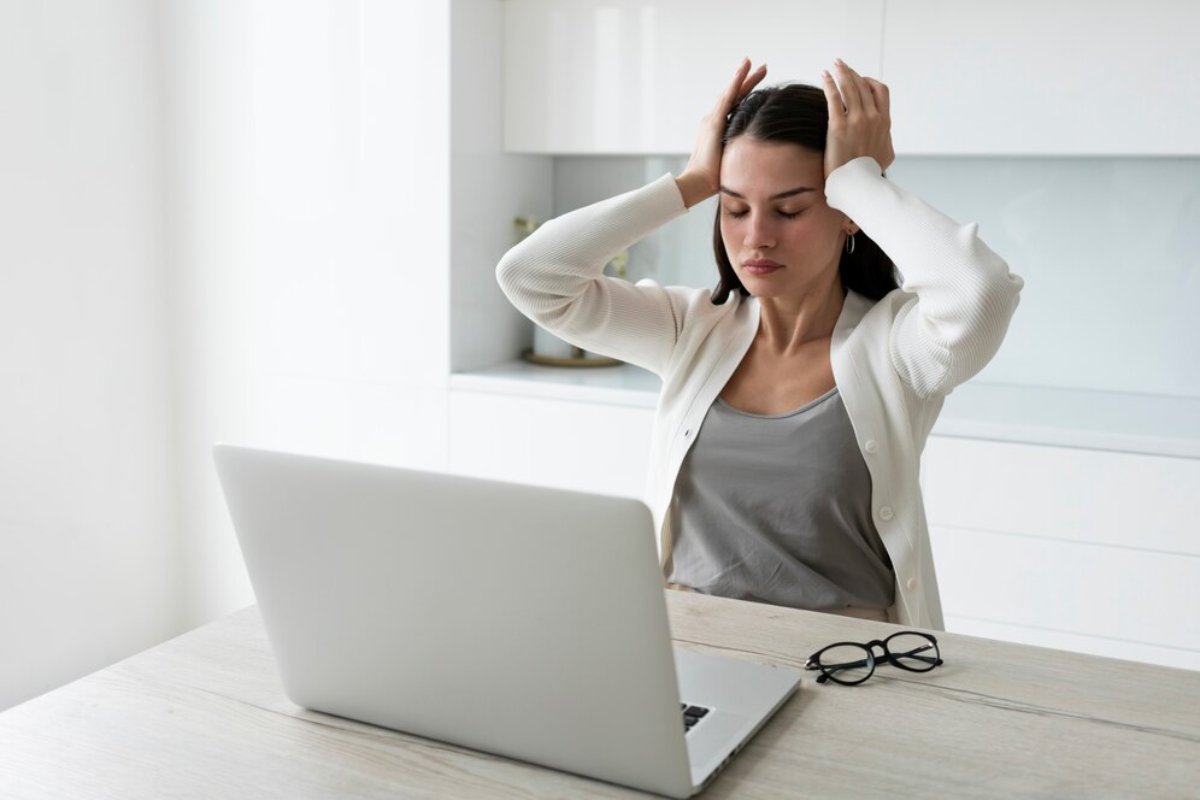 Woman feeling stressed or experiencing headache while working on laptop in a bright office.