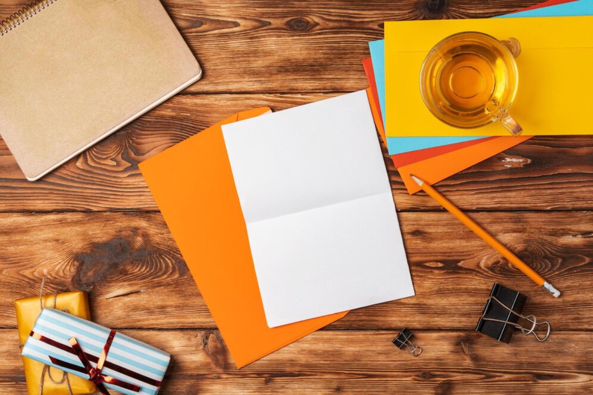 Top view of a wooden desk with colorful folders, a notebook, a cup of tea, and gift-wrapped boxes.