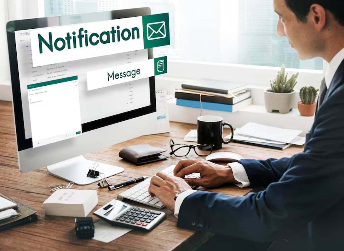 Man working at a desk with a computer displaying multiple email notification overlays.