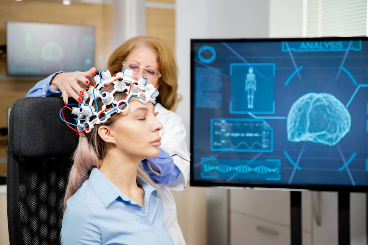 Woman undergoing a brain scan with a scientist adjusting a high-tech headgear, with brain imaging data displayed on a monitor.