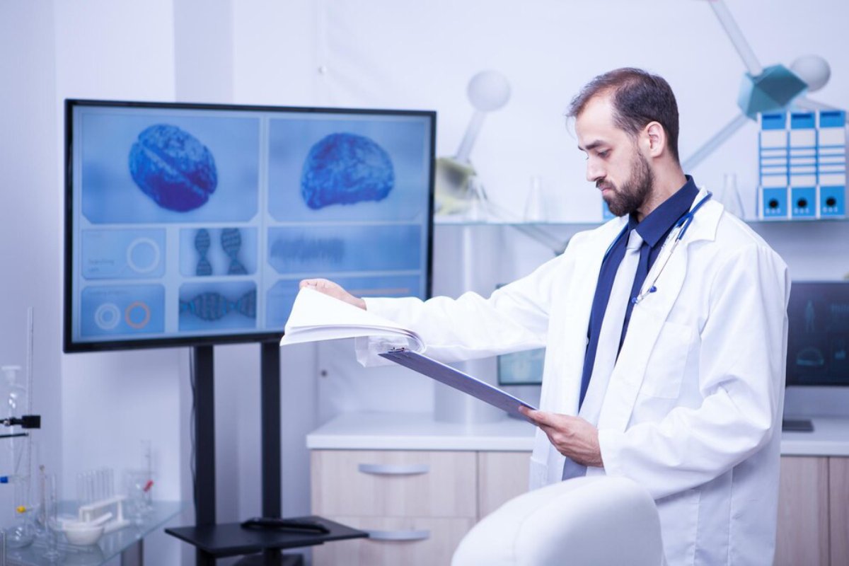 A male doctor examines a document in a lab with brain images on screens in the background.