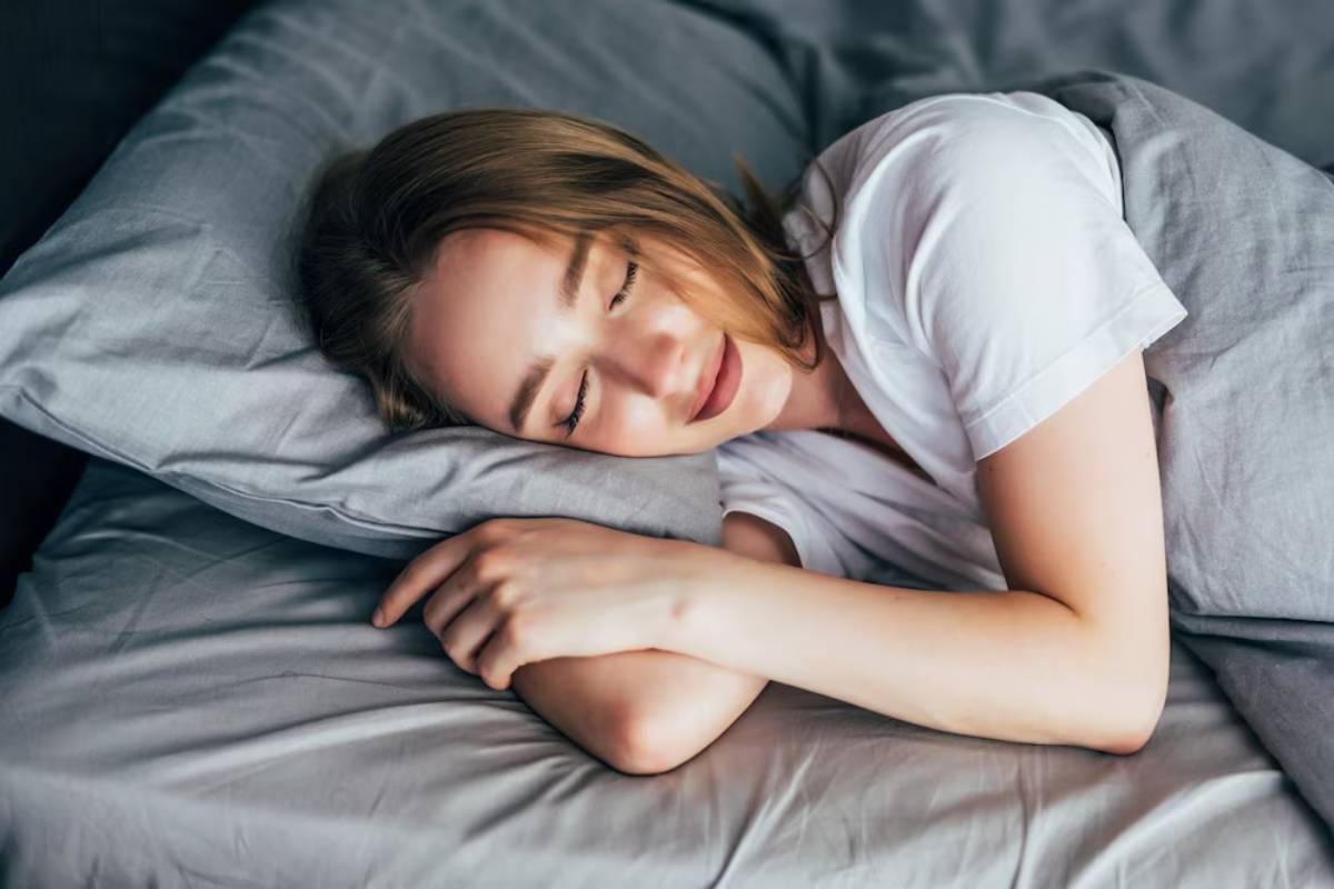 Young woman smiling peacefully while lying in bed, resting her head on a pillow.