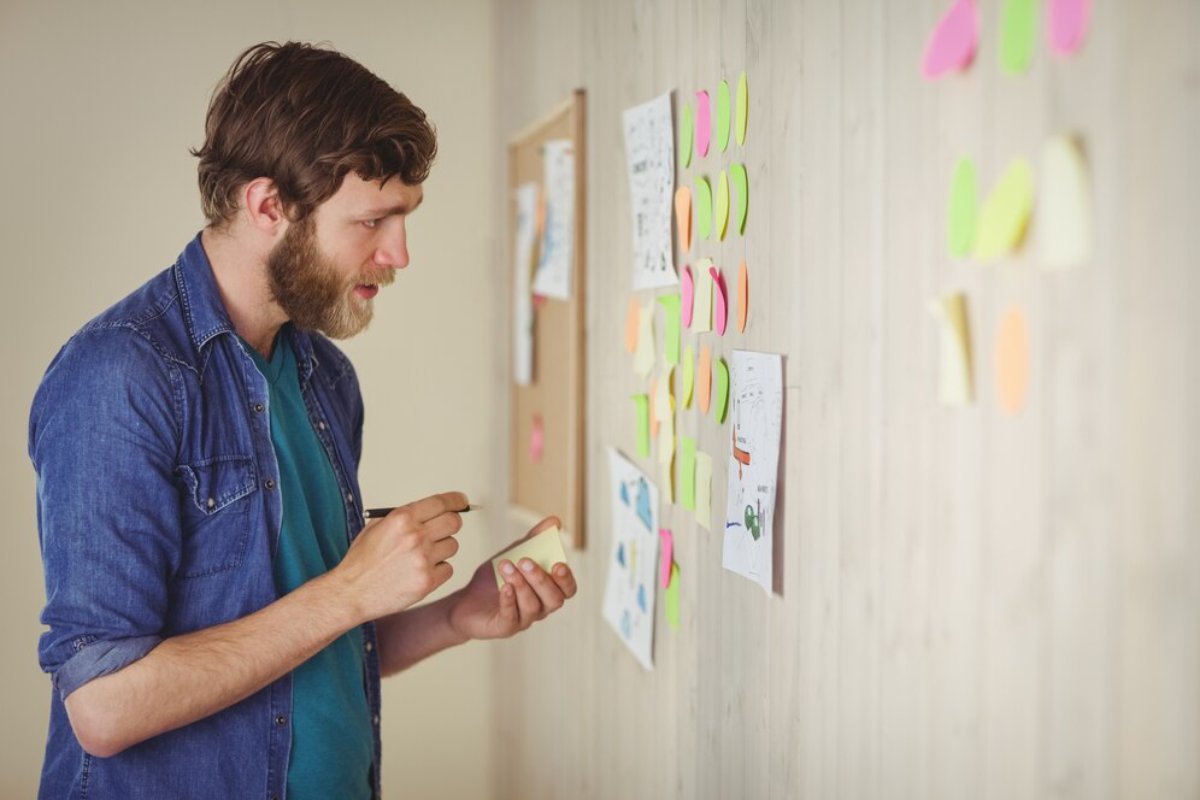Man in a denim shirt examining colorful sticky notes on a wall.