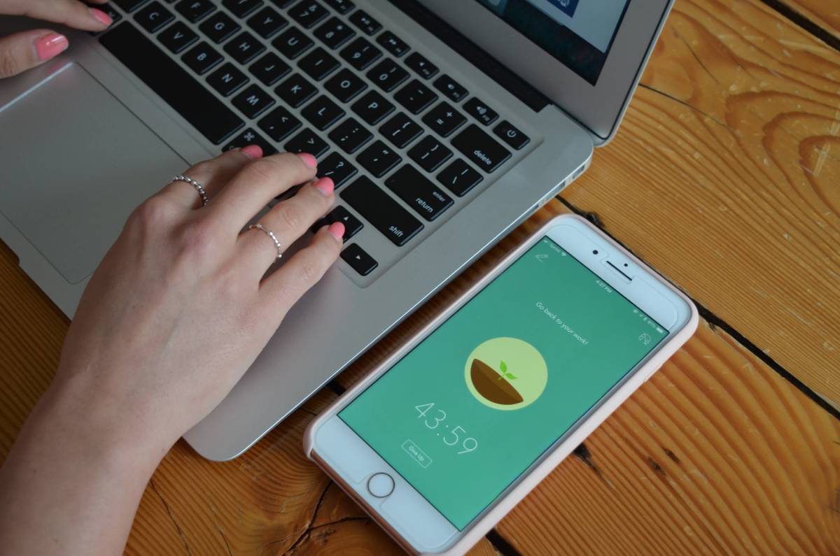 Hands typing on a laptop next to a smartphone displaying a health app timer on a wooden table.
