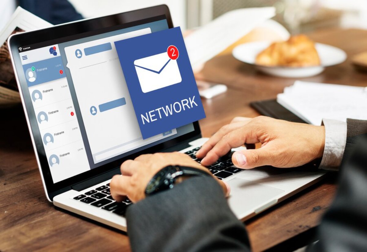 Businessman using a laptop displaying a social network and email notification interface in a meeting.