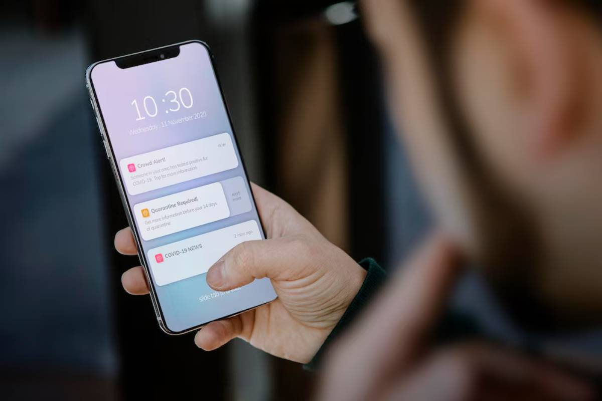 Person holding a smartphone displaying COVID-19 notifications and the time.