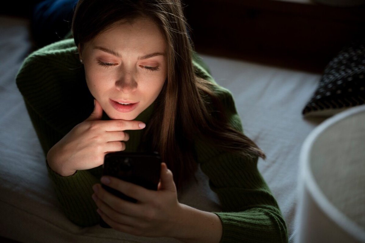 Young woman in a green sweater looking at her smartphone, appearing thoughtful and focused.