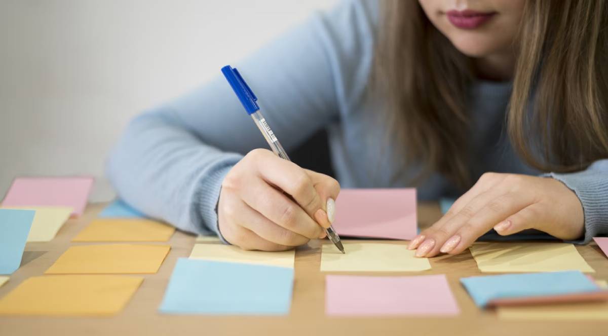 Woman writing on sticky notes with a blue pen at a desk.