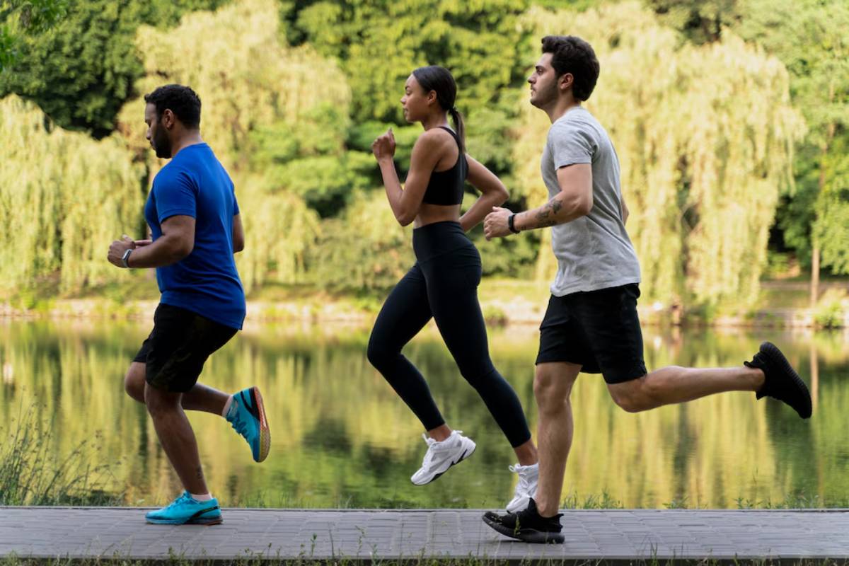 Three people jogging on a wooden pathway by a lake in a lush green park.