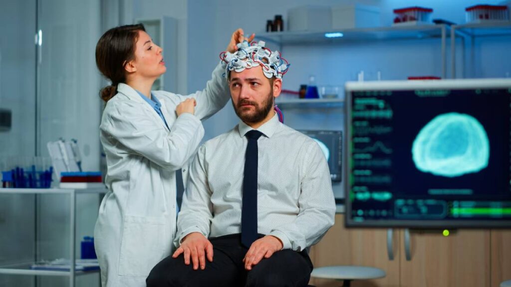 A female scientist adjusts a brain scanning device on a male participant in a laboratory.