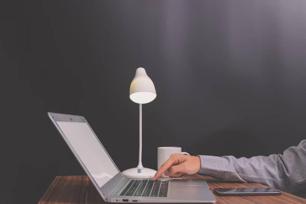 Person typing on a laptop under a lamp, with a dark background.