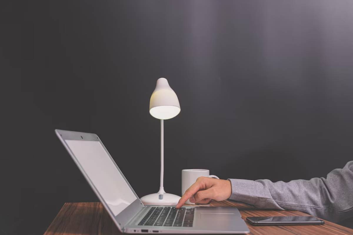 Person typing on a laptop under a lamp, with a dark background.