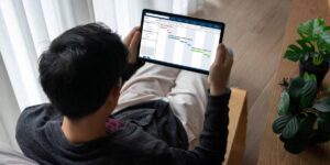 Man sitting on floor using tablet to view graphs, surrounded by indoor plants.