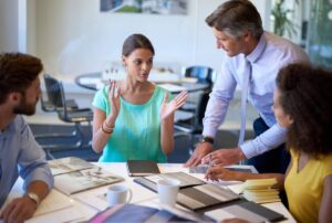 Four colleagues discuss plans around a table, with a woman gesturing animatedly.