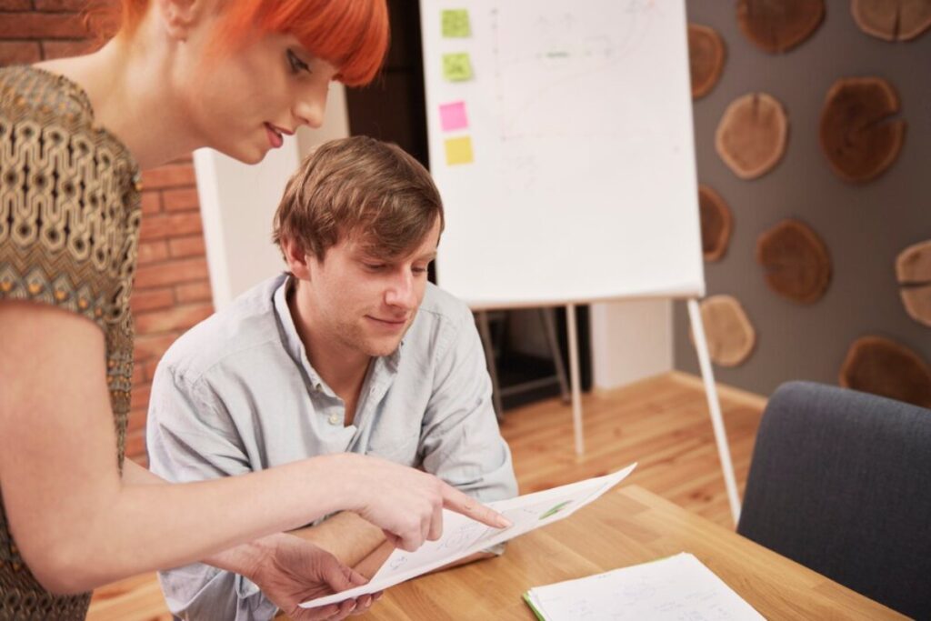 A woman with red hair and a man reviewing documents in a modern office setting.