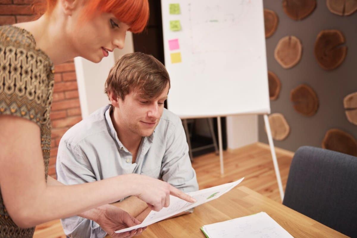 A woman with red hair and a man reviewing documents in a modern office setting.