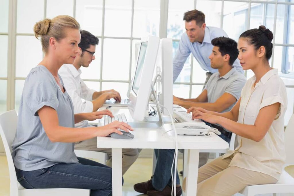 A group of four individuals works collaboratively at computers in a bright, modern office.