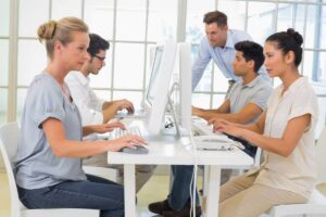 A group of four individuals works collaboratively at computers in a bright, modern office.