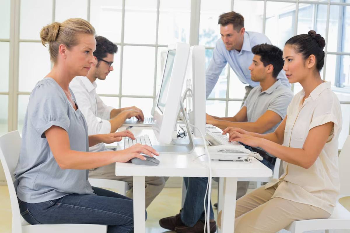 A group of four individuals works collaboratively at computers in a bright, modern office.